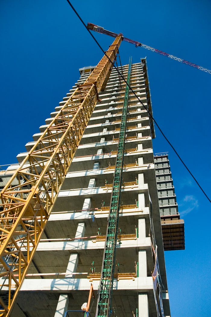 Low-angle view of skyscraper under construction with crane, clear blue sky.